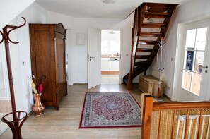 A hallway with a wooden floor, a red and blue patterned rug, a wooden cabinet, and a staircase with a wooden railing. - Close to the sea, quiet location - Reethaus Göhren FeWo 02 - Reethaus Göhren (Göhren)