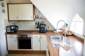 A compact kitchen with a coffee maker, a kettle, and a toaster on the countertop. There is a sink with a faucet and a window providing natural light.