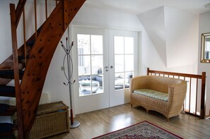 A room with a wooden staircase, a wicker sofa, a floor lamp, and a view through a door. - Close to the sea, quiet location - Reethaus Göhren FeWo 02 - Reethaus Göhren (Göhren)
