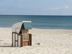 A beach chair with a striped cover, positioned on a sandy beach with the ocean in the background. - Close to the sea, quiet location - Reethaus Göhren FeWo 02 - Reethaus Göhren (Göhren)