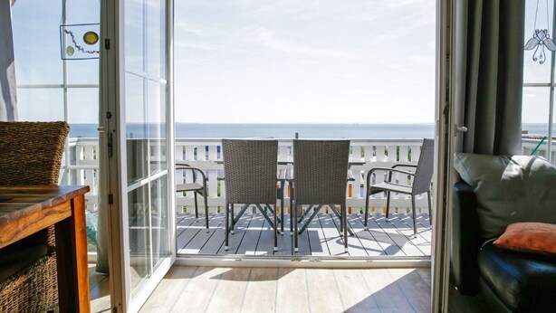Un balcon avec deux fauteuils en osier, une table en bois et une vue sur l’océan.