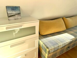 A bedroom with a white dresser, a plaid sofa with yellow cushions, and a framed picture on the dresser.