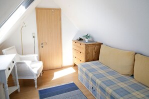 A dormitory room with a wooden wardrobe, a bed with plaid bedding, a white desk with drawers, a chair, and a small potted plant. - Close to the sea, quiet location - Reethaus Göhren FeWo 02 - Reethaus Göhren (Göhren)