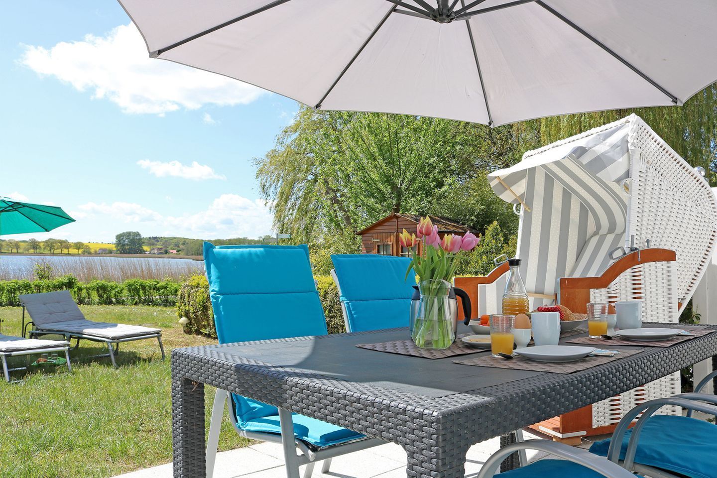 An outdoor dining area with a table set for breakfast, surrounded by blue chairs and a large umbrella.