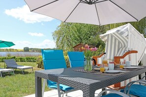 Un área de comedor al aire libre con una mesa dispuesta para el desayuno, rodeada de sillas azules y una sombrilla grande.