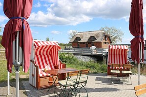 En restaurant ved floden med udendørs siddepladser, en bro og en bygning med stråtækt tag.