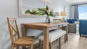 Een eethoek met een houten tafel, stoelen, een bank, een vaas met bloemen, een spiegel en een plafondventilator.