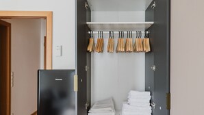 Ein begehbarer Kleiderschrank mit einem schwarzen Hisense-Kühlschrank, Holzkleiderbügeln und ordentlich gestapelten weißen Handtüchern.