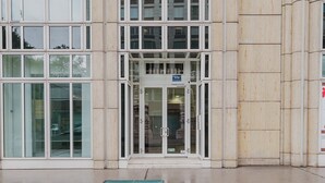 Ein Gebäudeeingang mit Glastür und einer Bank davor.