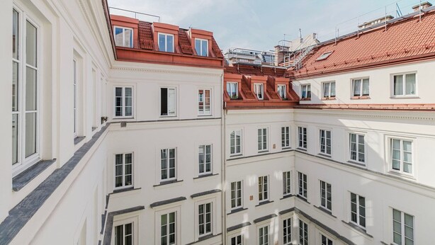 A multi-story building with white facades and red-tiled roofs, featuring multiple windows and balconies. - Upscale Neubau 3BR w/ Elevator & W/D, by Blueground (Vienna)