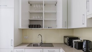 A modern kitchen with white cabinets, a stainless steel sink, and a countertop with a toaster, kettle, and coffee maker. - Upscale Neubau 3BR w/ Elevator & W/D, by Blueground (Vienna)