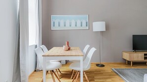 A modern living room with a wooden dining table, white chairs, a floor lamp, and a TV on a wooden stand. - Chic Döbling 1BR, Move-In-Ready w/ Furniture, by Blueground (Vienna)