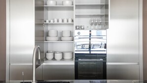 A stainless steel kitchen with built-in shelves for dishes and glasses, a built-in oven, and a stainless steel sink.