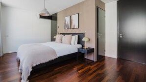 A modern bedroom with a large bed, a bedside table, a lamp, and a door.