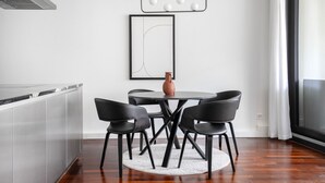 A modern dining area with a round table, four black chairs, a vase, and a minimalist light fixture.