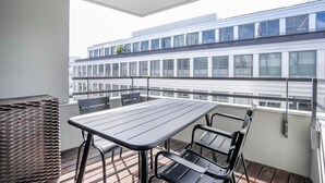 A balcony with a table and chairs, a wicker basket, and a view of a modern building with large windows.