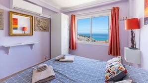 Une chambre à coucher avec un lit, une fenêtre avec des rideaux, un climatiseur fixé au mur et une étagère avec une lampe.