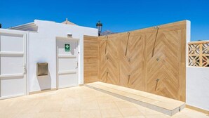 Un espace extérieur propre et moderne, agrémenté d’une clôture en bois, d’une porte blanche avec une enseigne verte et d’un sol carrelé.