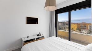 A modern bedroom with a large window, a bed, a bedside table, and a mounted TV. - Marinsa Beach,3 bed penthouse (Llanos, Los (Torrox-Costa))