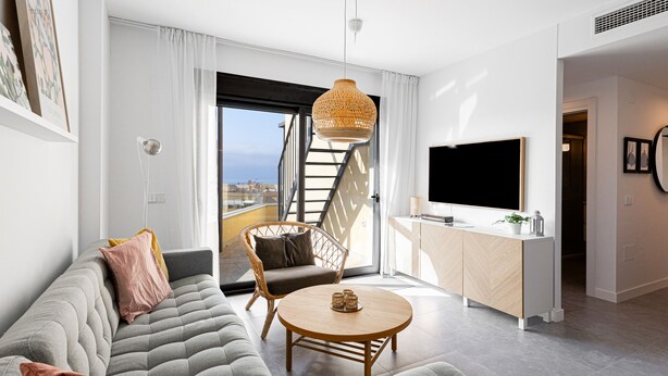 A modern living room with a sofa, a round coffee table, a wicker chair, a TV, and a staircase leading to a balcony. - Marinsa Beach,3 bed penthouse (Llanos, Los (Torrox-Costa))