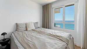A bedroom with a large bed, a nightstand, and a view of the sea through a window.
