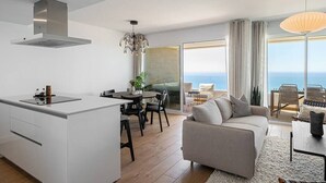A modern kitchen with a central island, dining area with chairs, a sofa, and a view of the ocean through large windows. - Isea Calaceite, 2 bedroom (Llanos, Los (Torrox-Costa))