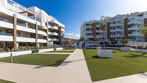 A modern apartment complex with multiple balconies, a central pathway, and landscaped areas with artificial grass and planters. - Isea Calaceite, 2 bedroom (Llanos, Los (Torrox-Costa))