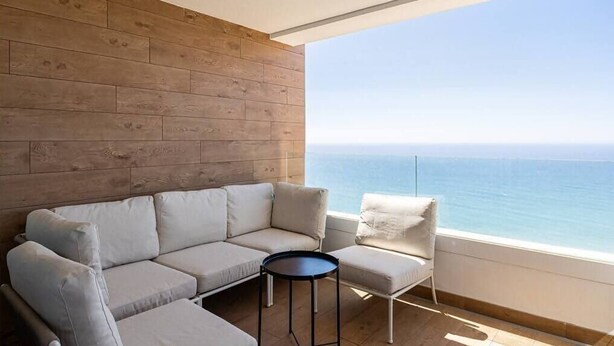 A modern living room with a wooden wall, a beige sofa, a small round table, and a view of the sea. - Isea Calaceite, 2 bedroom (Llanos, Los (Torrox-Costa))