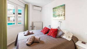 A bedroom with a bed, pillows, a bedside table, a nightstand, an air conditioning unit, a window with curtains, and a painting on the wall. - Albaida, 1 bedroom with balcony (Nerja)