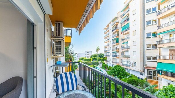 A balcony with a glass table and chairs, surrounded by lush greenery and adjacent multi-story buildings. - Albaida, 1 bedroom with balcony (Nerja)