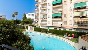 A swimming pool surrounded by a residential building with balconies, a clear sky, and palm trees. - Albaida, 1 bedroom with balcony (Nerja)