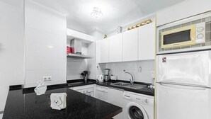 A modern kitchen with white cabinets, a black countertop, a washing machine, a microwave, and a refrigerator. - Albaida, 1 bedroom with balcony (Nerja)