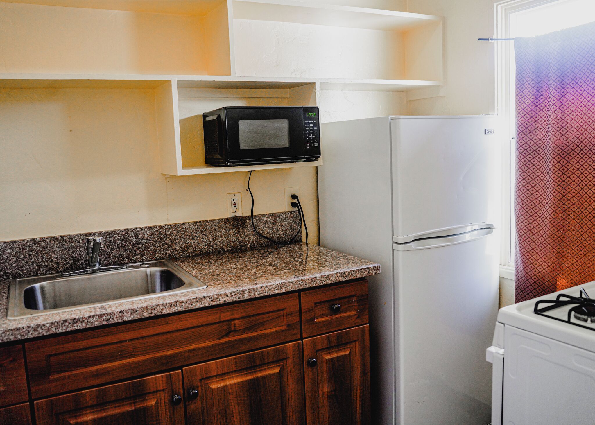 A kitchen with granite countertops, wooden cabinets, a white refrigerator, a microwave, and a gas stove.