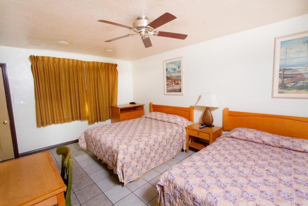 A hotel room with two beds, a ceiling fan, a desk, and a chair.