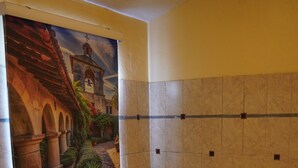 Un bany amb una banyera gran, parets revestides de rajoles i un mural que mostra un pati d'interior.