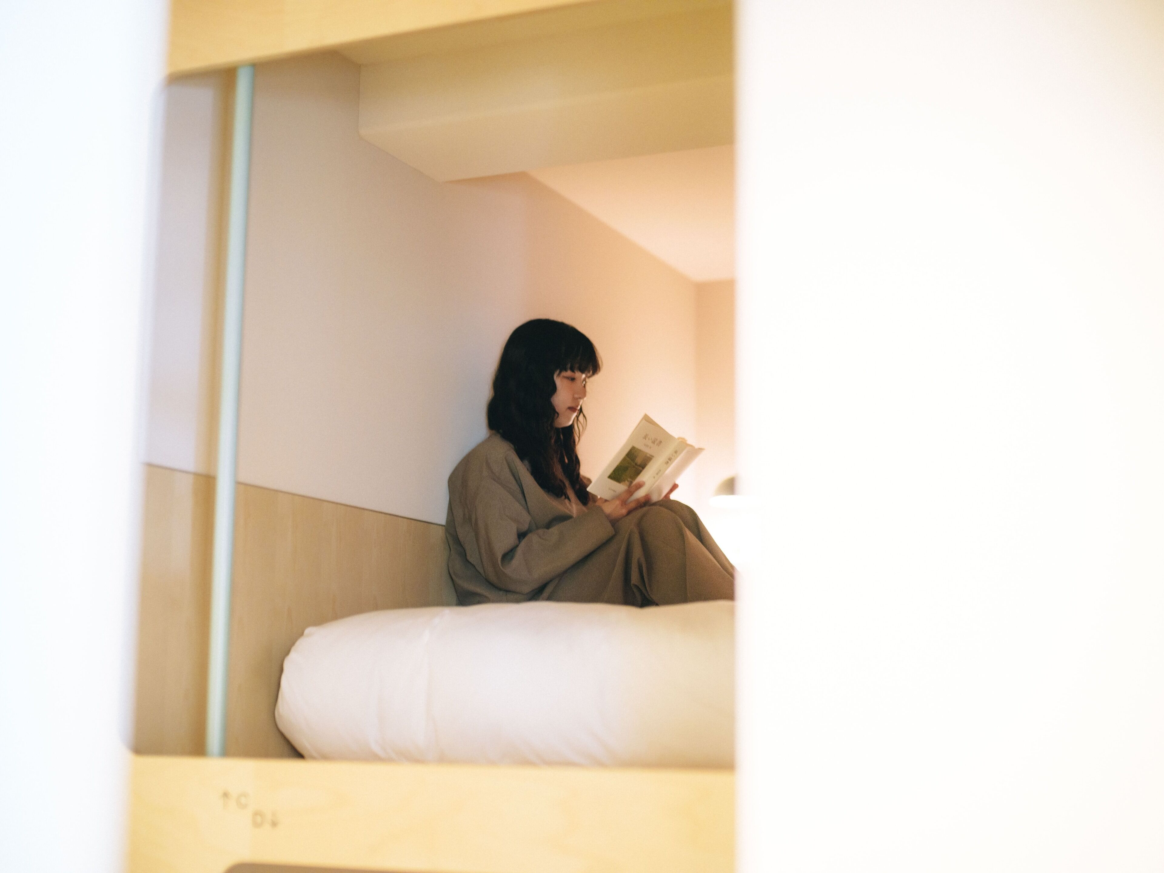 A person sitting on a white bed in a room with a wooden headboard and a plain wall.