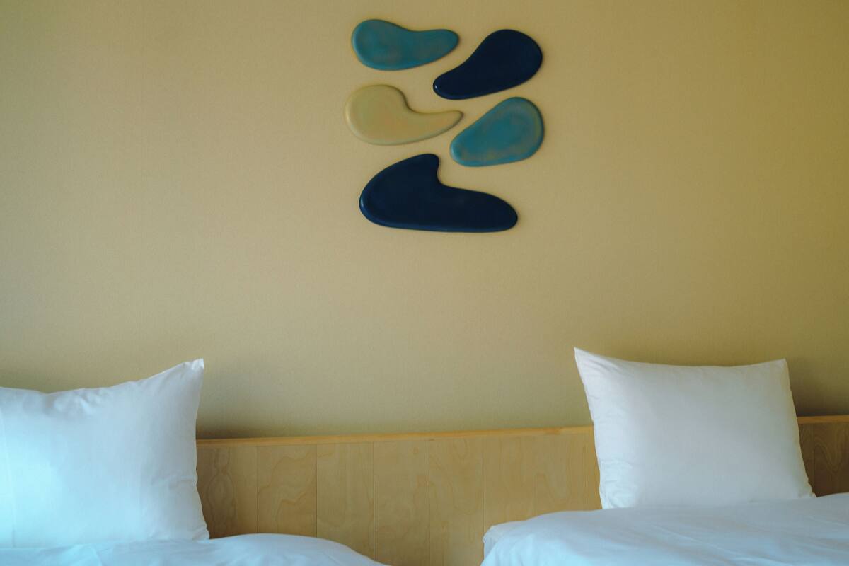 A hotel room with two beds, a wooden headboard, and a wall with abstract art.