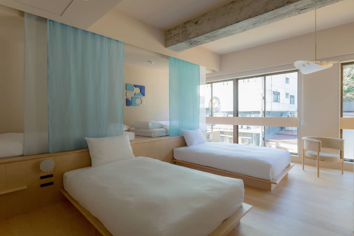 A modern hotel room with two beds, a large window, and a view of the city.