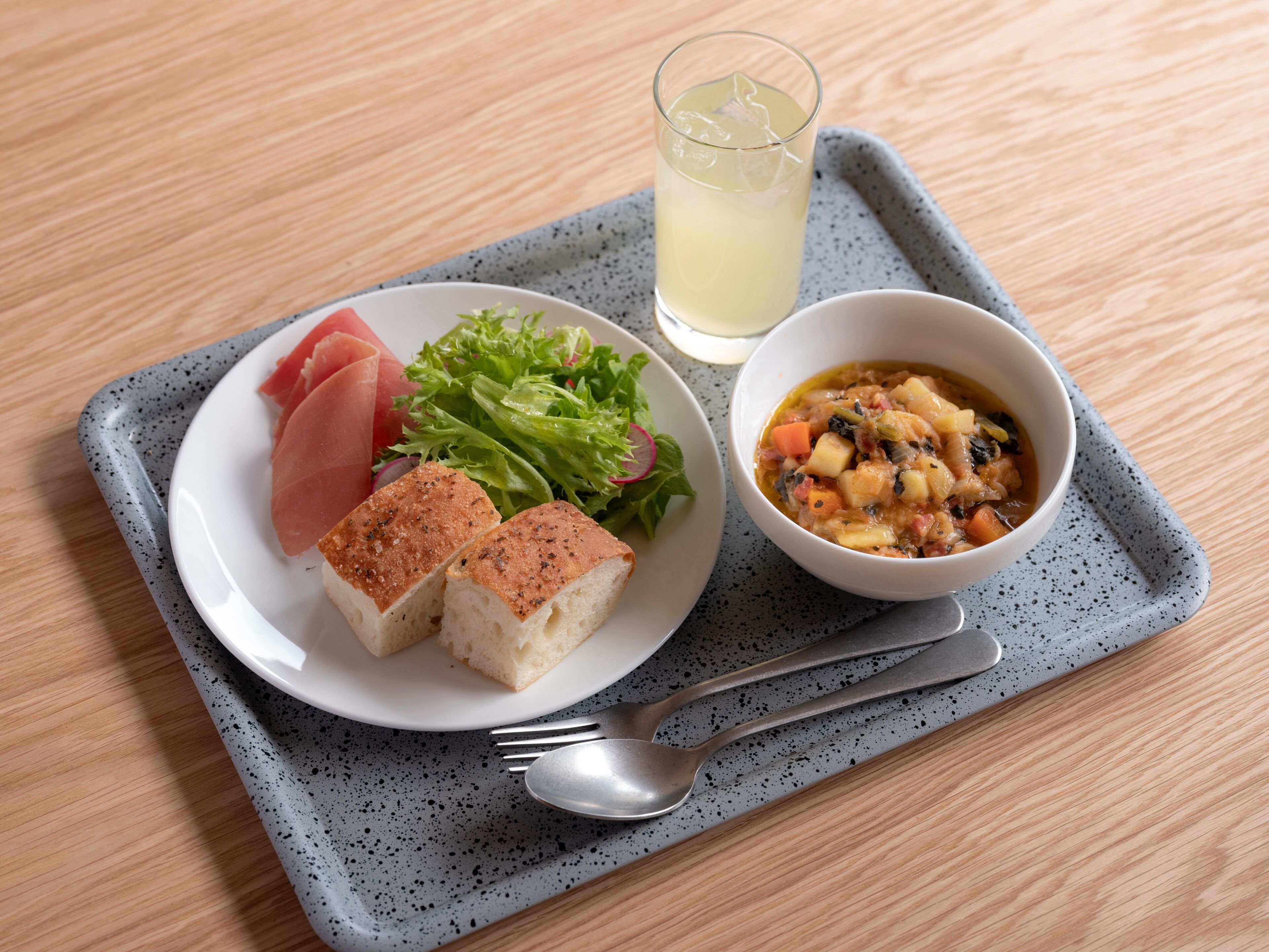 A meal tray with a plate of food, including bread, salad, and a bowl of soup, on a speckled gray tray.