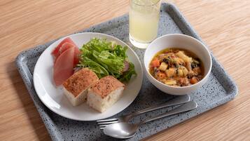 A meal tray with a plate of food, including bread, salad, and a bowl of soup, on a speckled gray tray.