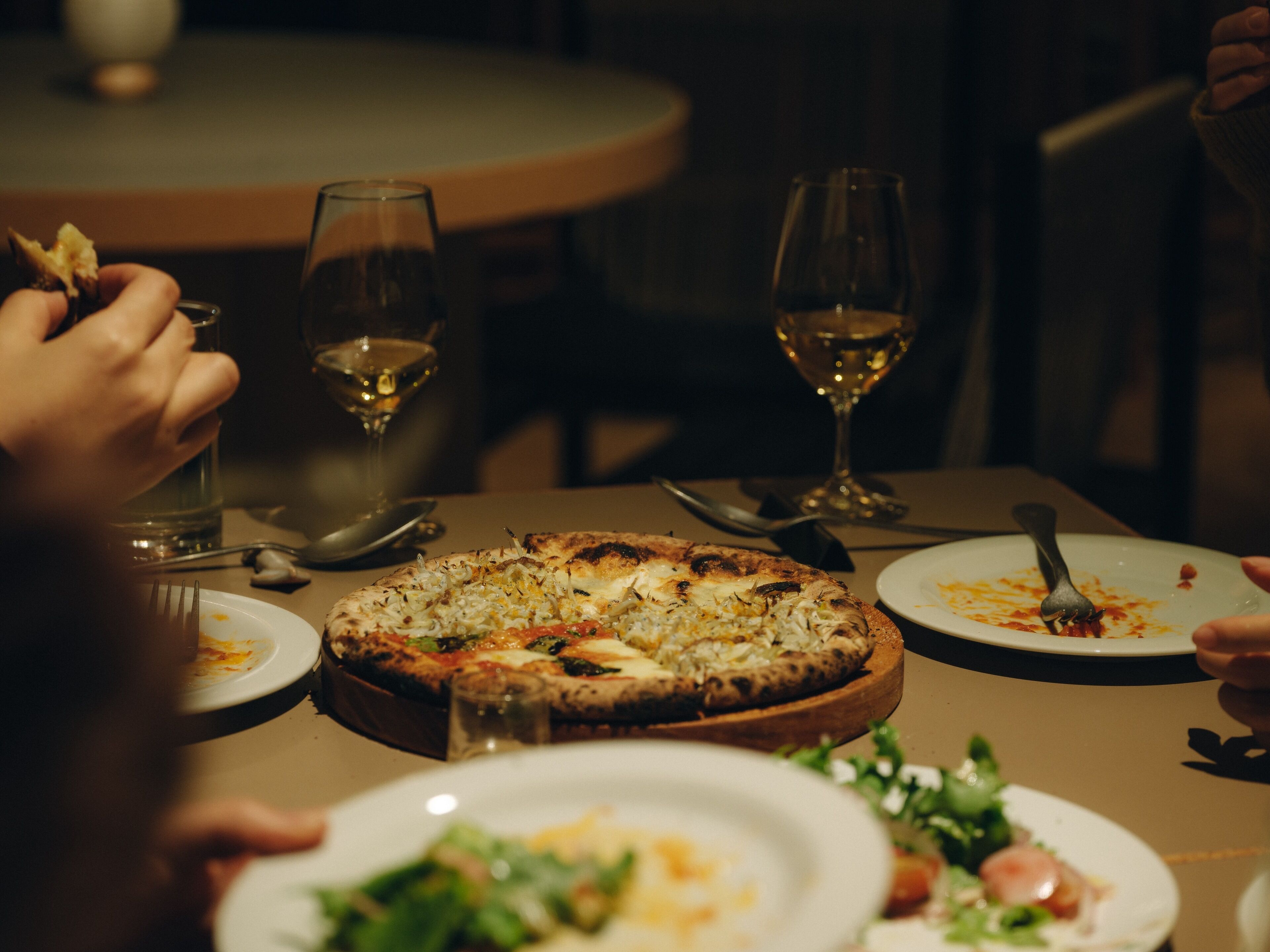 Una mesa de comedor con pizza, copas de vino y platos.