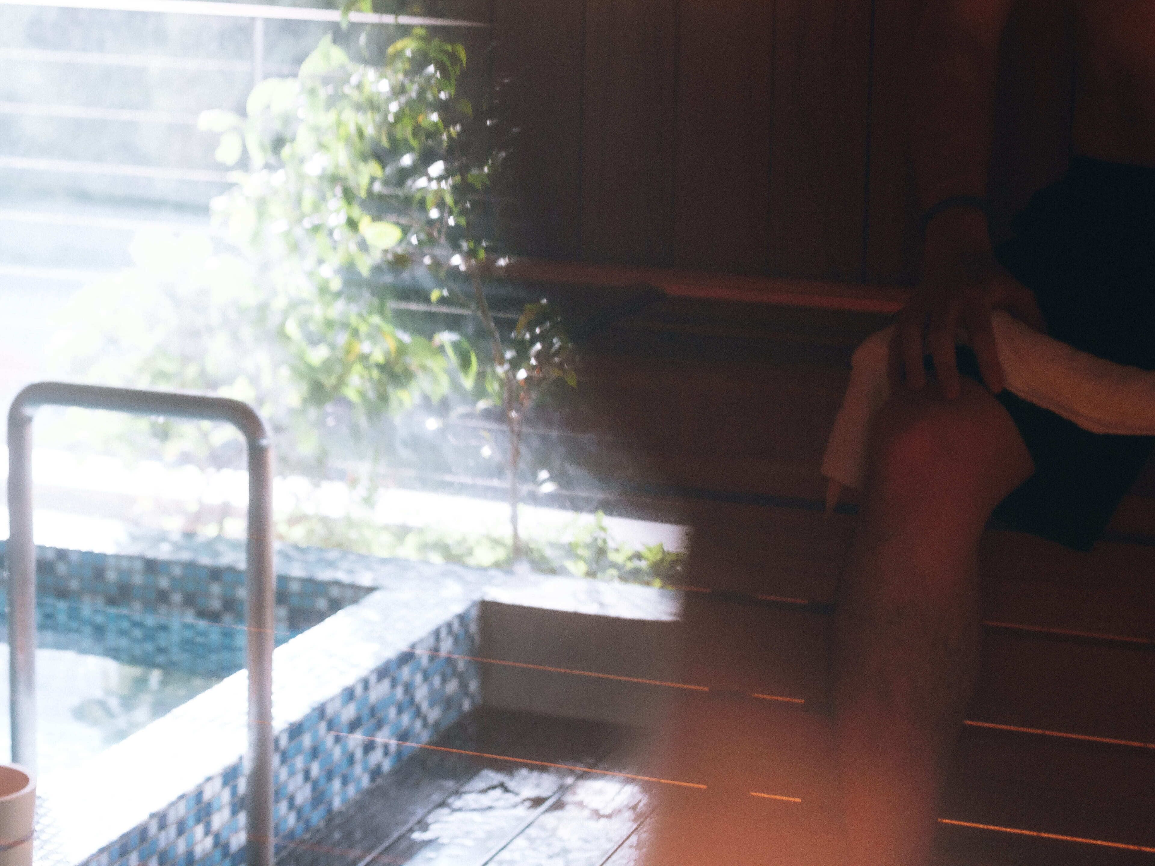 A person sitting by a window with a view of a pool and greenery.