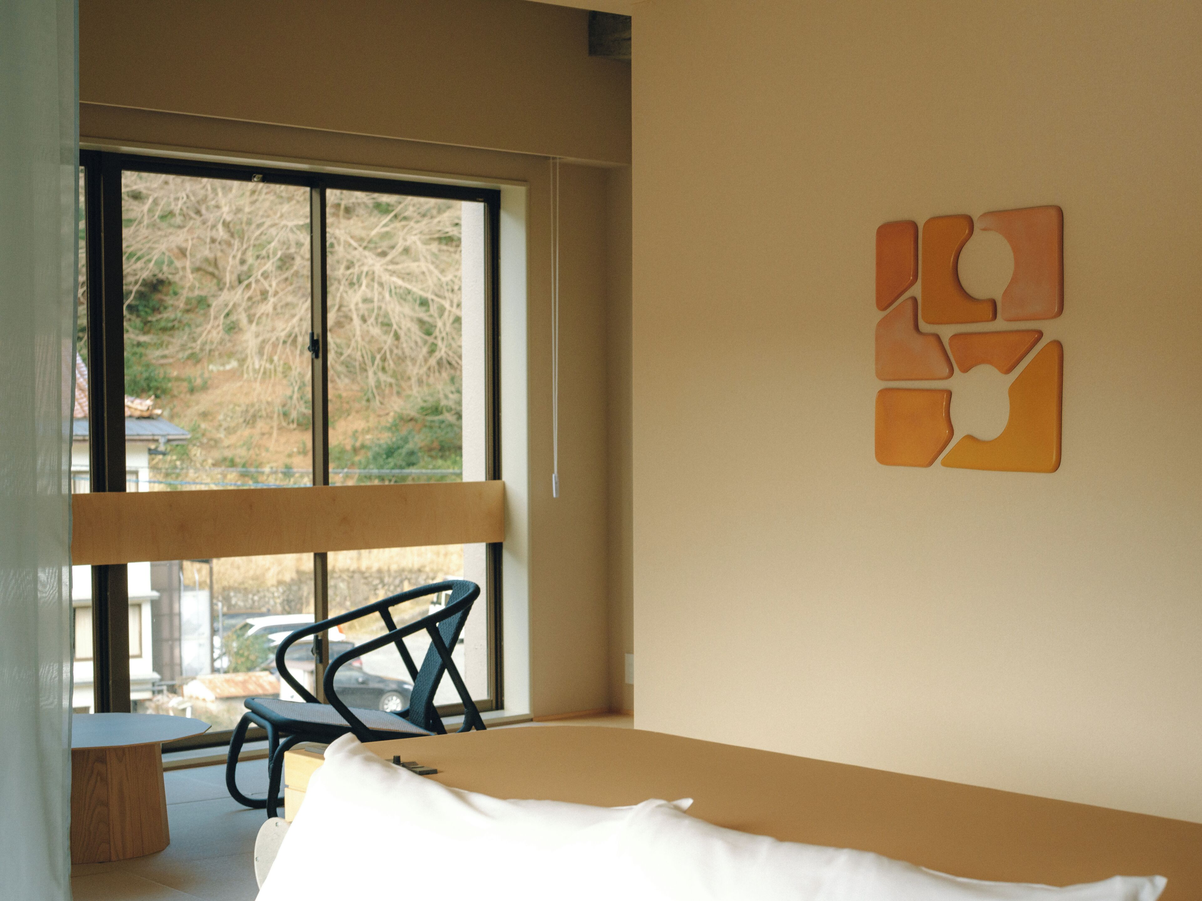 A bedroom with a bed, a chair, a window, and a wall with a geometric decoration.