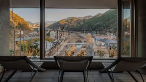 Habitación con un amplio ventanal que da a un paisaje montañoso y un río. Se observan dos sillas en primer plano.
