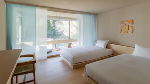Une chambre d’hôtel moderne, dotée de deux lits, d’un bureau et d’une grande fenêtre donnant sur un paysage verdoyant.