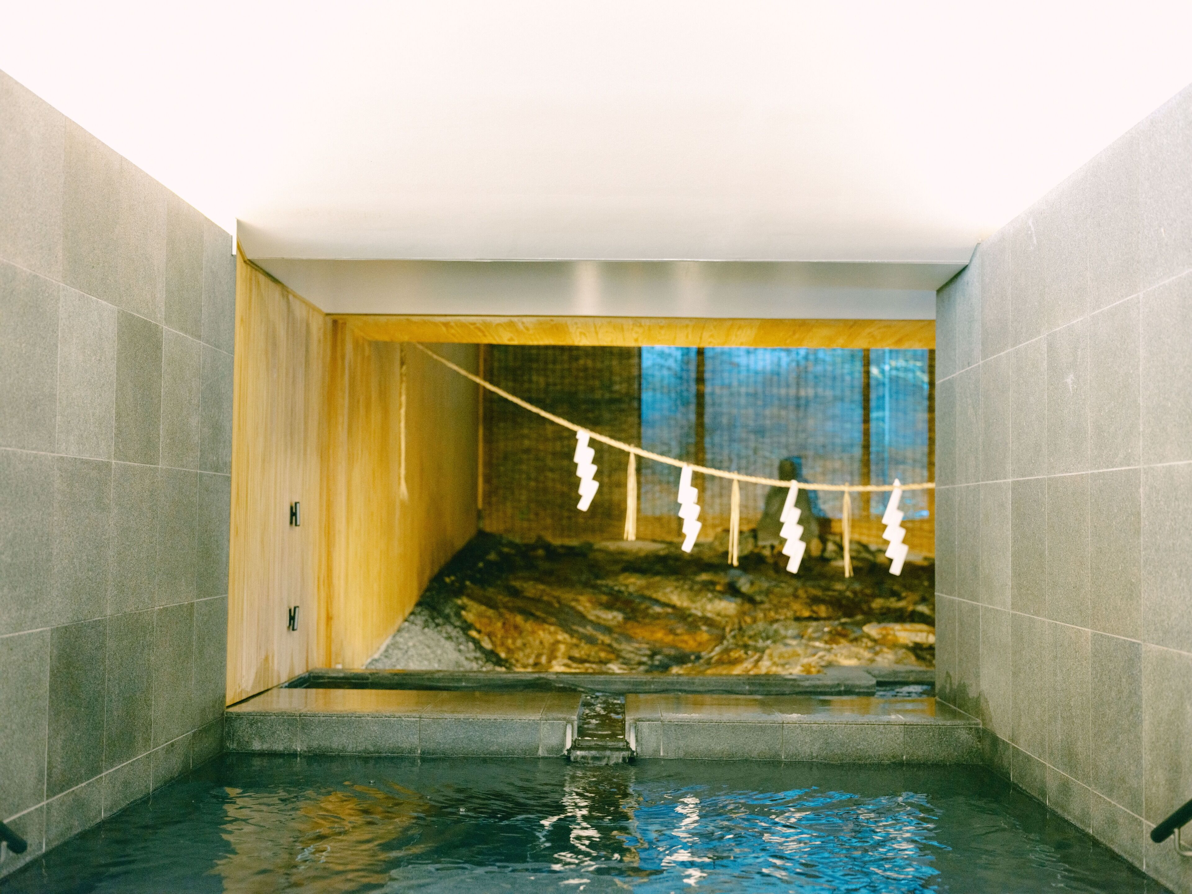 Un moderno cuarto de spa con pared de piedra, un banco de madera y una cuerda de toallas blancas colgando del techo.
