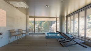 Un espace piscine intérieur moderne, doté d’un plancher en bois, de chaises longues et d’une piscine aux carreaux bleus.