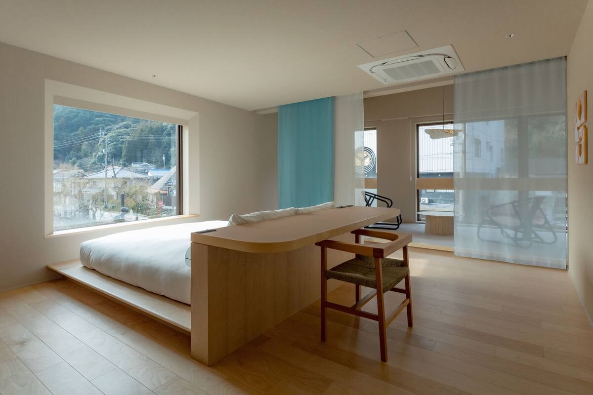 A modern bedroom with a large bed, a small desk, and a view of the outside.
