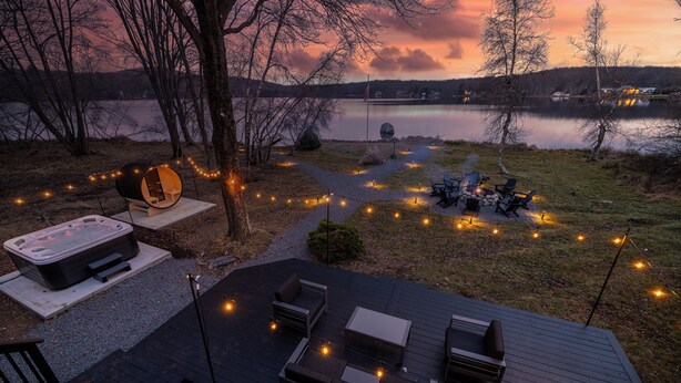 A deck with outdoor seating, a hot tub, and string lights. - Arrowhead Premier Lakefront w/Sauna, Hot Tub, Firepit, Game Room, Amenities, (Pocono Lake)