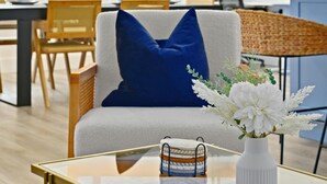 A modern living room with a glass coffee table, a blue cushion, and a white vase with flowers. - Designer Home,  Sleep 8,  Ask us about FREE add-ons (Austin)